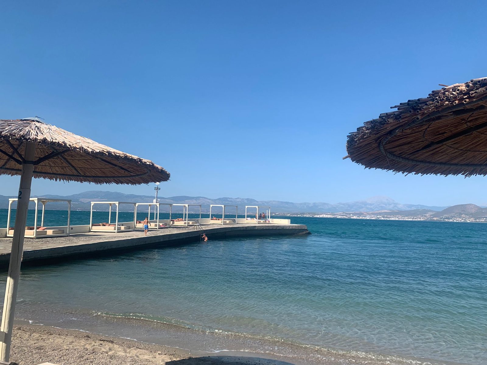 החוף הצמוד למלון Brown Beach Chalkida, מזח עם מיטות שיזוף ושמשיות קש